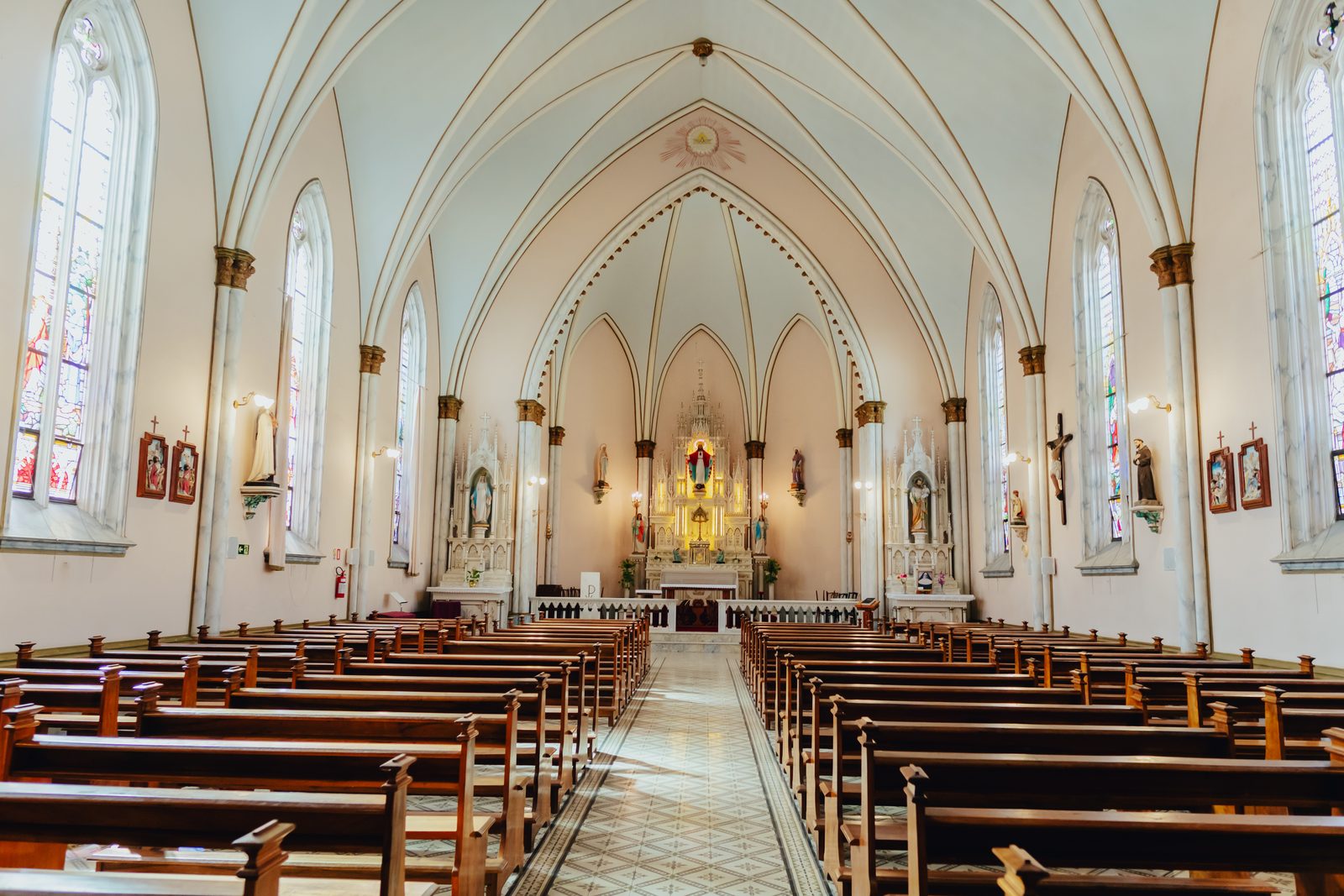 Interior da capela do Mosteiro, com arcos góticos, vitrais e bancos de madeira